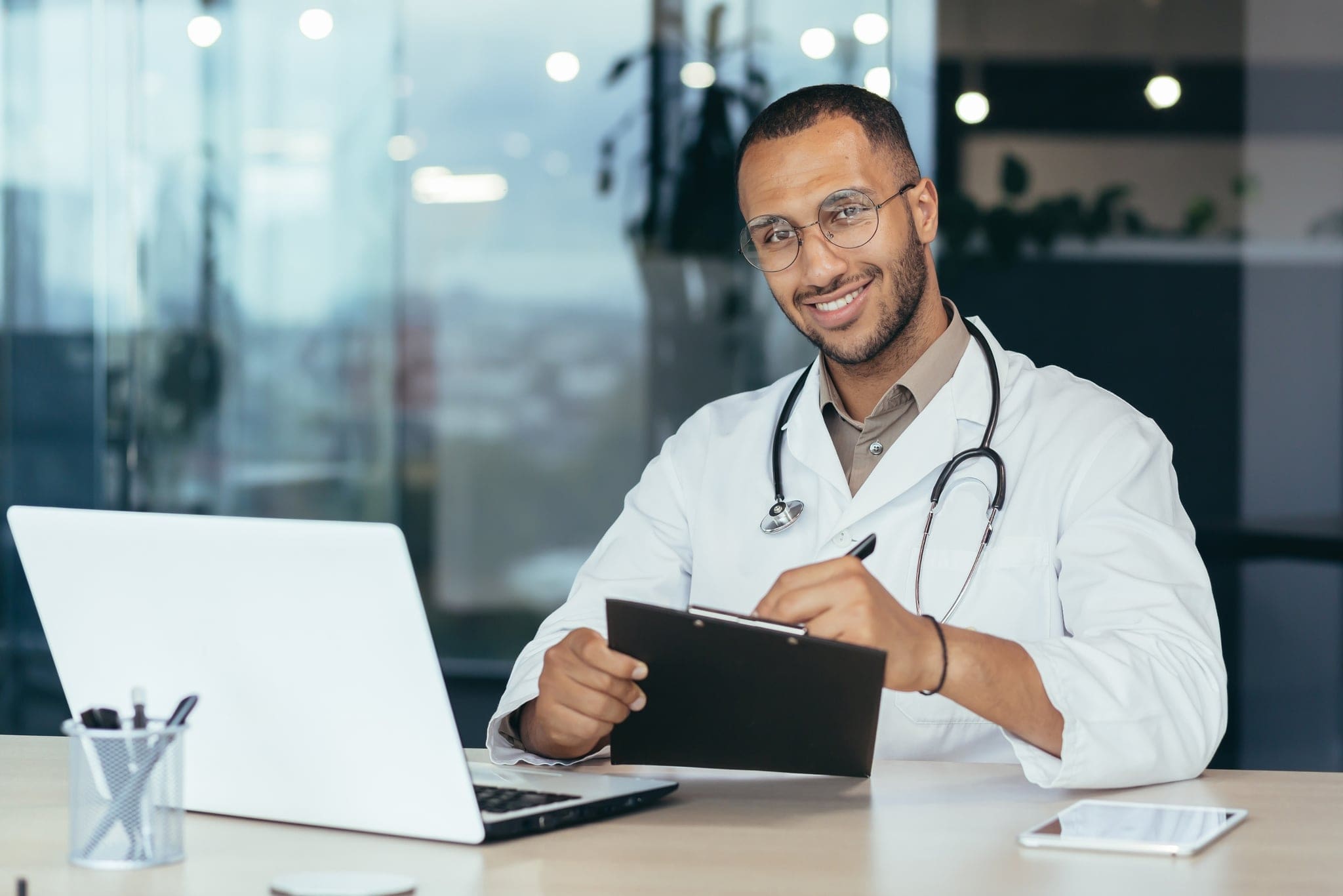 Male doctor smiling and looking at camera, using laptop for work.